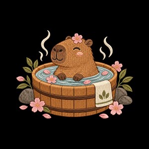 Può includere: Un disegno ricamato che raffigura un capibara marrone che si rilassa in un tino di legno rotondo pieno d'acqua. La scena include fiori di ciliegio rosa, foglie verdi, pietre grigie e un asciugamano bianco drappeggiato sul lato con vapore.