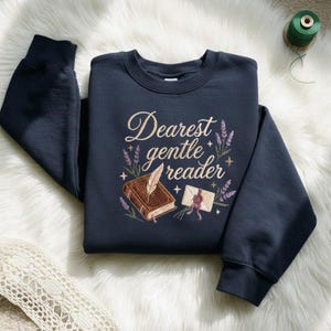Może przedstawiać: Granatowa bluza z haftowanym napisem "Dearest gentle reader". Projekt zawiera książkę, pióro, kopertę, lawendę i gwiazdy. Bluza ma okrągły dekolt.
