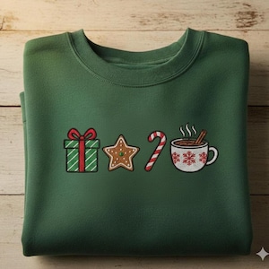 Puede incluir: Sudadera verde oscuro con diseños bordados con temática navideña. Los diseños incluyen un regalo envuelto, una galleta de jengibre en forma de estrella, un bastón de caramelo y una taza de chocolate caliente con copos de nieve y una rama de canela.