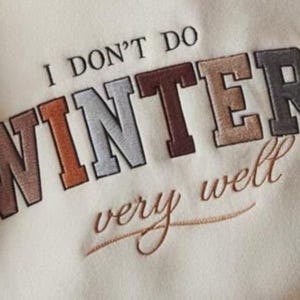 Puede incluir: Sudadera color crema con la frase bordada "I DON'T DO WINTER very well." El texto est&aacute; en una mezcla de colores, incluyendo marr&oacute;n, naranja, gris y beige. La sudadera tiene un estilo casual y relajado.