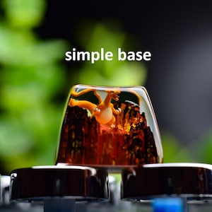 May include: A custom keycap with an orange dragon figure set against a fiery background. The keycap is clear with a simple base design and the text "simple base" in white. The keycap is mounted on a keyboard.