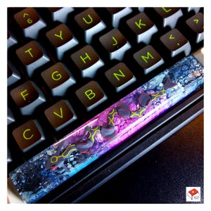 Puede incluir: Un teclado con una tecla de resina colorida. La tecla presenta un patrón de remolino de azul, rosa y negro con un diseño amarillo y gris.