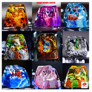 Puede incluir: Nueve teclas diferentes con varios personajes de Pokémon encapsulados en resina transparente. Cada tecla presenta un personaje de Pokémon diferente y una escena de fondo única. Las teclas están todas en una formación de cuadrícula, con tres filas y tres columnas.