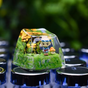 May include: A custom keycap with a miniature forest scene inside, including a cartoon character, trees, and mushrooms. The clear keycap sits on a keyboard. The diorama is highly detailed. The keycap is a unique decorative item.