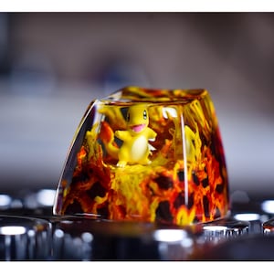 May include: A yellow and orange resin keycap with a small yellow Pokemon character inside. The keycap is clear and shows the character in detail.