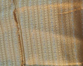 Pode incluir: Close-up de um tecido dourado com um padrão detalhado. O design apresenta listras verticais com elementos florais e geométricos em uma sequência repetitiva. O tecido tem um leve brilho.