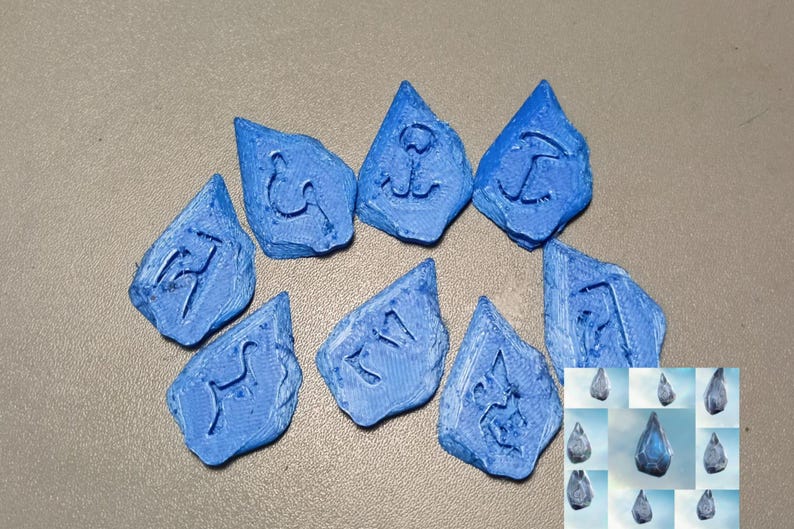 Puede incluir: Nueve piedras azules de forma irregular con s&iacute;mbolos grabados. Las piedras est&aacute;n dispuestas sobre una superficie neutra. Una imagen m&aacute;s peque&ntilde;a de piedras similares est&aacute; en la esquina inferior derecha. Los s&iacute;mbolos parecen ser de tem&aacute;tica n&aacute;utica o mar&iacute;tima.