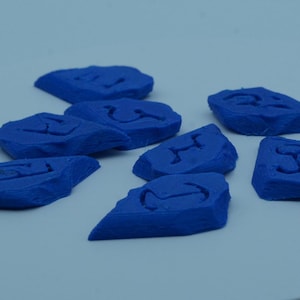 Puede incluir: Un conjunto de objetos azules de forma irregular, cada uno con un s&iacute;mbolo tallado. Los objetos est&aacute;n dispersos sobre una superficie azul claro. Los s&iacute;mbolos son dise&ntilde;os abstractos.