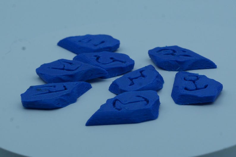 Puede incluir: Un conjunto de objetos azules de forma irregular, cada uno con un s&iacute;mbolo tallado. Los objetos est&aacute;n dispersos sobre una superficie azul claro. Los s&iacute;mbolos son dise&ntilde;os abstractos.