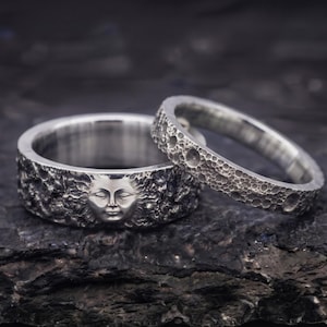 Può includere: Due anelli in argento con finitura testurizzata. L'anello più largo presenta un design in rilievo di un volto solare dettagliato con occhi chiusi e raggi. L'anello più stretto ha una superficie butterata e craterizzata simile alla luna.