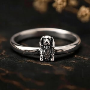 Könnte beinhalten: Ein silberner Ring mit einer detaillierten Hundefigur. Der Hund steht im Mittelpunkt, auf einem polierten Band. Das Design des Rings ist aufwendig und zeigt die Merkmale des Hundes. Silberring.