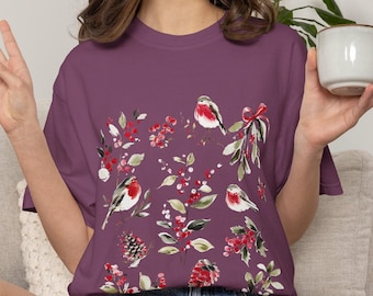 May include: A berry-colored short-sleeve t-shirt featuring a watercolor-style print of three small birds with red chests, green holly leaves, red berries, and pinecones. The text Color Berry is printed in the upper left corner of the image.
