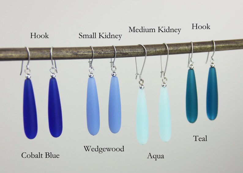 May include: Six pairs of teardrop-shaped glass earrings in various shades of blue, including cobalt blue, wedgewood, aqua, and teal. The earrings are displayed on a wooden dowel with the hook style and kidney wire style earring findings.