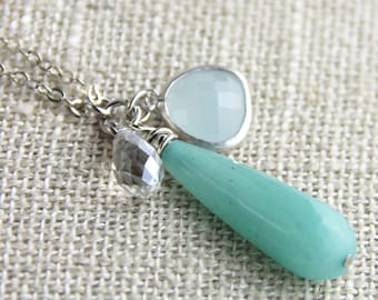 May include: A silver chain necklace with a turquoise teardrop pendant, a clear crystal pendant, and a light blue gemstone pendant.