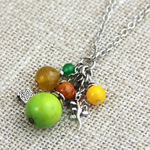 May include: A silver chain necklace with a charm featuring a green, yellow, and brown bead cluster, a silver lizard charm, and a silver decorative charm.