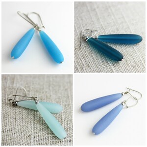 May include: Four pairs of dangle earrings with silver hooks and frosted glass teardrop-shaped beads. The earrings are in shades of blue, teal, and aqua.