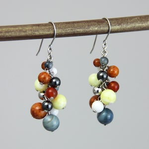 May include: A pair of dangle earrings with a cluster of colorful beads. The beads are in shades of brown, red, yellow, white, and blue. The earrings are made with silver-toned metal.