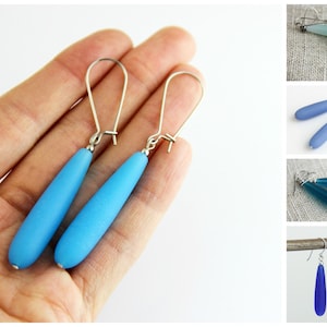 May include: A pair of dangle earrings with teardrop-shaped blue glass beads and silver hooks.