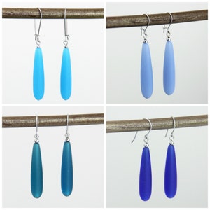 May include: Four pairs of teardrop-shaped glass earrings in various shades of blue. The earrings are silver and dangle from a hook.