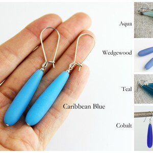 May include: A pair of dangle earrings with silver hooks and teardrop-shaped glass beads in various shades of blue, including aqua, Wedgwood, teal, Caribbean blue, and cobalt.