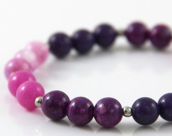 May include: A purple and pink ombre beaded bracelet with silver metal spacers. The bracelet is made with round beads that are graduated in size.