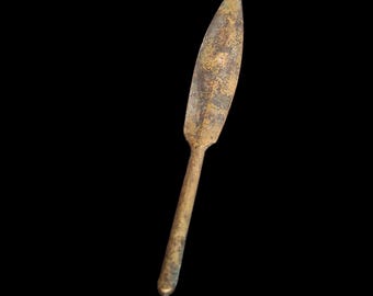 May include: A small, antique bronze knife with a pointed blade and a long, slender handle. The metal has a weathered, aged appearance with areas of discoloration, suggesting its age and use. The knife is set against a solid black background.