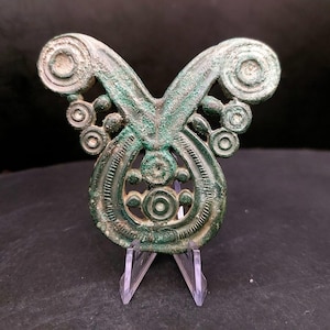 Peut inclure: Broche antique en bronze avec un design complexe. La broche présente une forme centrale en goutte d'eau avec des détails circulaires et en spirale, et deux bras incurvés avec des extrémités en spirale. Le métal a un aspect vieilli.