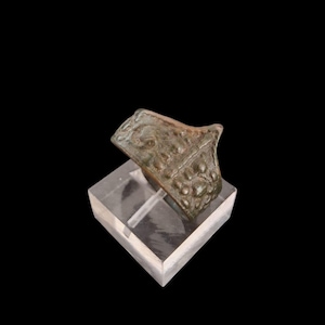 May include: A bronze-colored ring with a textured surface, displayed on a clear acrylic stand against a black background. The ring's design features raised, rounded details. The ring appears to be an antique or vintage piece.