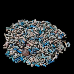May include: A large collection of small, cylindrical and spherical beads in various shades of blue, white, and tan. The assortment includes matte, weathered textures and smooth, glossy finishes, with one translucent, amber-coloured bead included.