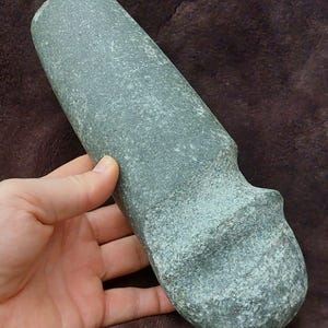 Puede incluir: Un hacha de mano de piedra lisa, de color verde, con una cabeza redondeada y un extremo ligeramente puntiagudo.