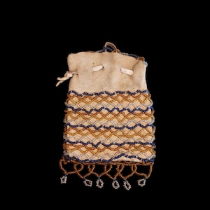 Può includere: Un piccolo astuccio in pelle bianco sporco con chiusura a coulisse. La parte inferiore è decorata con un motivo ripetuto di perline blu e oro. Il bordo inferiore presenta frange di perline pendenti.