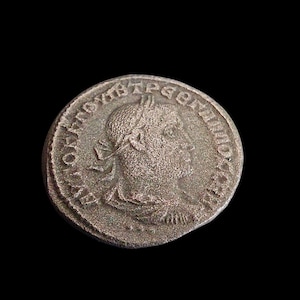 Puede incluir: Una moneda de plata con un retrato de perfil y inscripciones. La moneda muestra signos de desgaste, con detalles de la cara y el texto aún visibles. El fondo es negro liso.