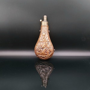 Könnte beinhalten: Antike kupferfarbene Flasche mit aufwendigen floralen und heraldischen Reliefschnitzereien. Die Flasche hat einen silberfarbenen Deckel mit einem kleinen Hebel und einen abgerundeten Boden. Das detaillierte Design deutet auf einen historischen oder dekorativen Gegenstand hin.