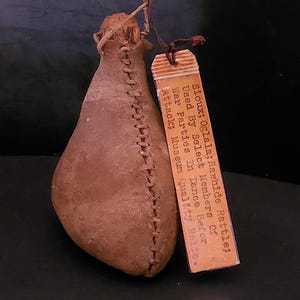 Peut inclure: Un hochet en peau brute marron avec une couture cousue sur le côté. Une petite étiquette est attachée avec le texte "Sioux; Oglala; Rawhide Rattle; Used By Select Members Of War Parties In Dance Before Attack; Museum Quality Relic."