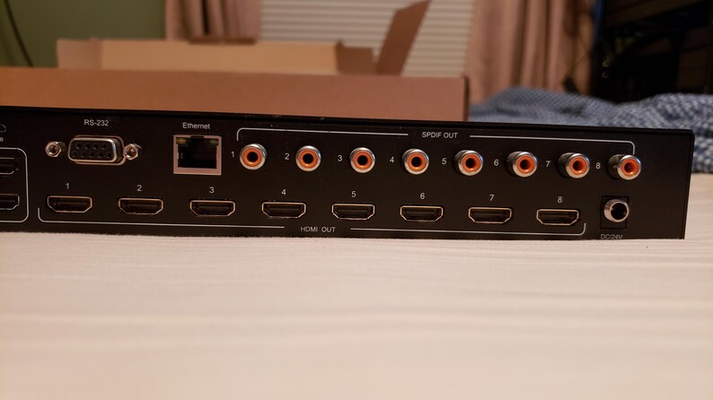 Puede incluir: Dispositivo electr&oacute;nico negro con m&uacute;ltiples puertos de salida HDMI y audio. Cuenta con conexiones RS-232, Ethernet y SPDIF OUT. El dispositivo tiene una entrada de CC y est&aacute; dise&ntilde;ado para aplicaciones audiovisuales.