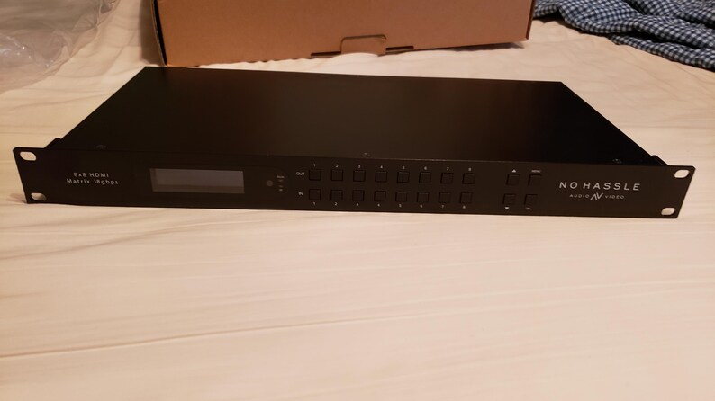 Puede incluir: Un conmutador matricial HDMI 8x8 negro con una pantalla y varios botones. El texto "NO HASSLE Audio/Video" est&aacute; impreso en el lado derecho. El dispositivo es rectangular y tiene orificios de montaje.