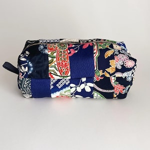 Può includere: Un beauty case rettangolare patchwork con chiusura a zip e un piccolo passante in tessuto. La borsa è realizzata con vari tessuti fantasia nei toni del blu, rosso e bianco. La borsa misura circa 20 cm di lunghezza e 10 cm di altezza.