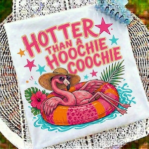 May include: White t-shirt with a graphic of a flamingo wearing sunglasses and a straw hat, floating in an orange and pink inner tube. The text "HOTTER THAN A HOOCHIE COOCHIE" is printed above the flamingo in pink.