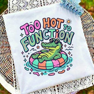 May include: White t-shirt featuring a cartoon alligator wearing sunglasses, floating on a striped inflatable ring. The text "Too Hot to Function" is above the alligator. The design is in pink, orange, and teal.