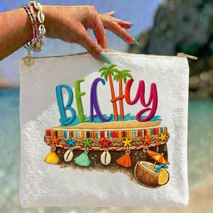 Könnte beinhalten: Weiße Reißverschlusstasche mit dem Wort "BEACHY" in bunten 3D-Buchstaben. Das Design umfasst eine Strandszene mit Palmen, einem Kokosnussgetränk und dekorativen Quasten. Die Tasche wird von einer Hand mit einem Armband gehalten.