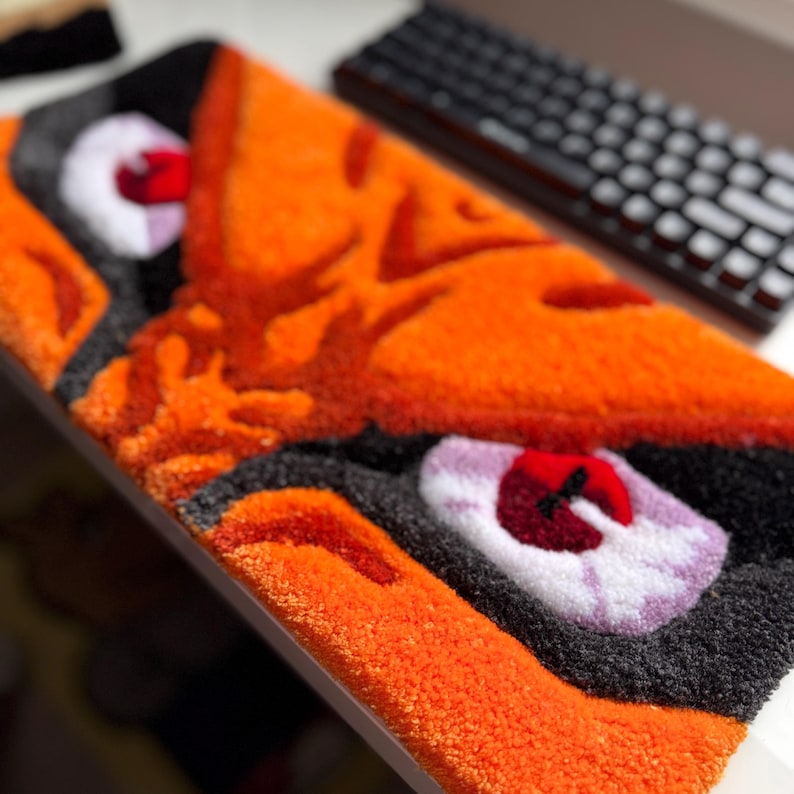 Keyboard rug with a vibrant orange anime face design. The rug features black, white, and red accents, creating a striking contrast. The plush texture and bold colors make it a decorative piece.