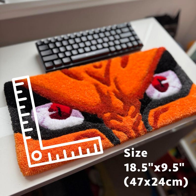 May include: Orange and black rug with a tiger face design. The rug measures 18.5" x 9.5". The eyes are white with red pupils. The rug has a textured appearance and is rectangular. A black keyboard is in the background.