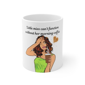 Może przedstawiać: Biały ceramiczny kubek do kawy z ilustracją w stylu pop-art kobiety z rudymi włosami i zielonym topem, trzymającej filiżankę kawy. Na kubku widnieje napis "Little miss can't function without her morning coffee".