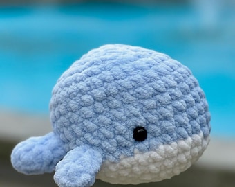 May include: A handmade, plush whale toy in shades of blue and white. The whale has a rounded body, small flippers, and a black eye. The soft, textured material gives it a cuddly appearance. The toy is designed to be a child's toy.