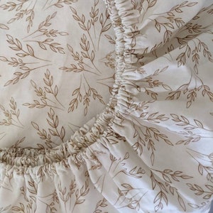 May include: A close-up of a fitted sheet with a white background and a brown floral pattern. The sheet has an elastic band around the edge.