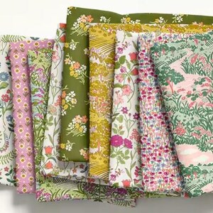May include: A collection of folded fabric pieces featuring various floral and landscape patterns. The fabrics display a range of colors, including pink, green, yellow, and blue, with detailed botanical designs. The fabrics are likely for sewing or crafting.