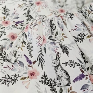 May include: White fabric with a floral pattern featuring pink flowers, green leaves, and black and white rabbits.