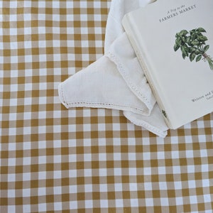 Puede incluir: Un mantel de lino blanco con un patrón de cuadros marrones y blancos. Un libro blanco con el título "A Trip to the Farmers Market" está sobre el mantel.