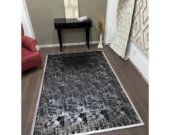 Könnte beinhalten: Ein rechteckiger Teppich mit einem abstrakten Muster in Schwarz und Silber. Der Teppich hat eine strukturierte Oberfläche, einen gemusterten Rand und eine weiße Umrandung. Er liegt auf einem Holzboden.