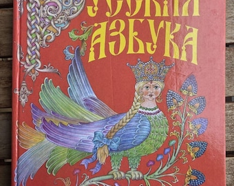 Puede incluir: Un libro de tapa dura con cubierta roja que presenta una colorida ilustración de una criatura mítica, una mujer con cuerpo de ave que lleva una corona. El texto cirílico "РУССКАЯ АЗБУКА" aparece en letras amarillas grandes arriba y "Просвещение" abajo.